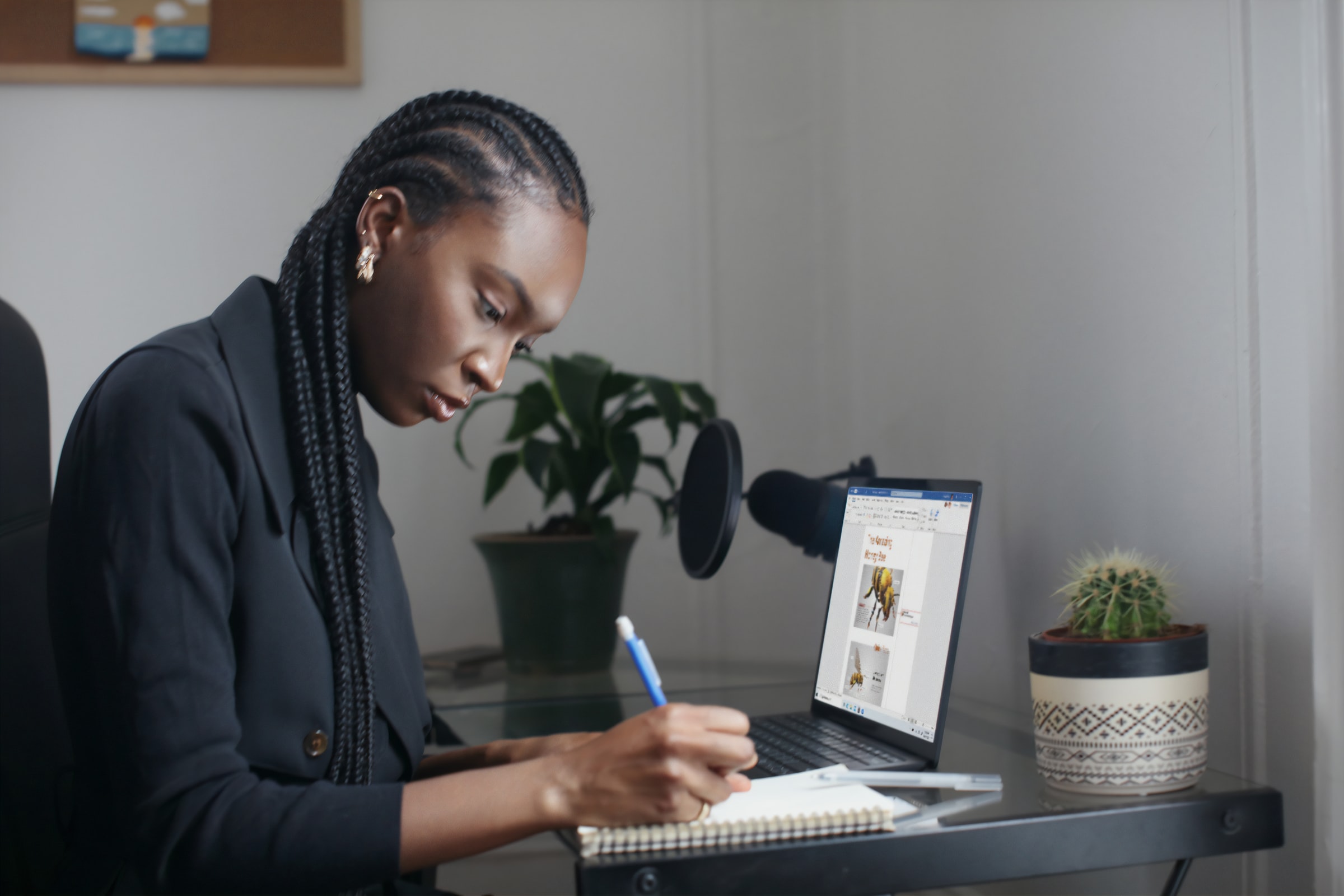 Vemos uma mulher, negra, empresaria, fazendo algumas anotações em seu escritório home office (imagem ilustrativa). Texto: negócios de impacto.
