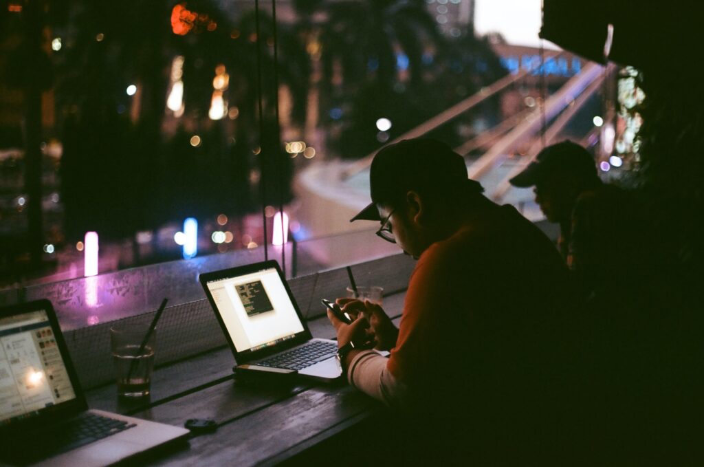 Vemos um homem sentado à mesa de um café; vemos também notebooks, celulares e copos ao redor (imagem ilustrativa).