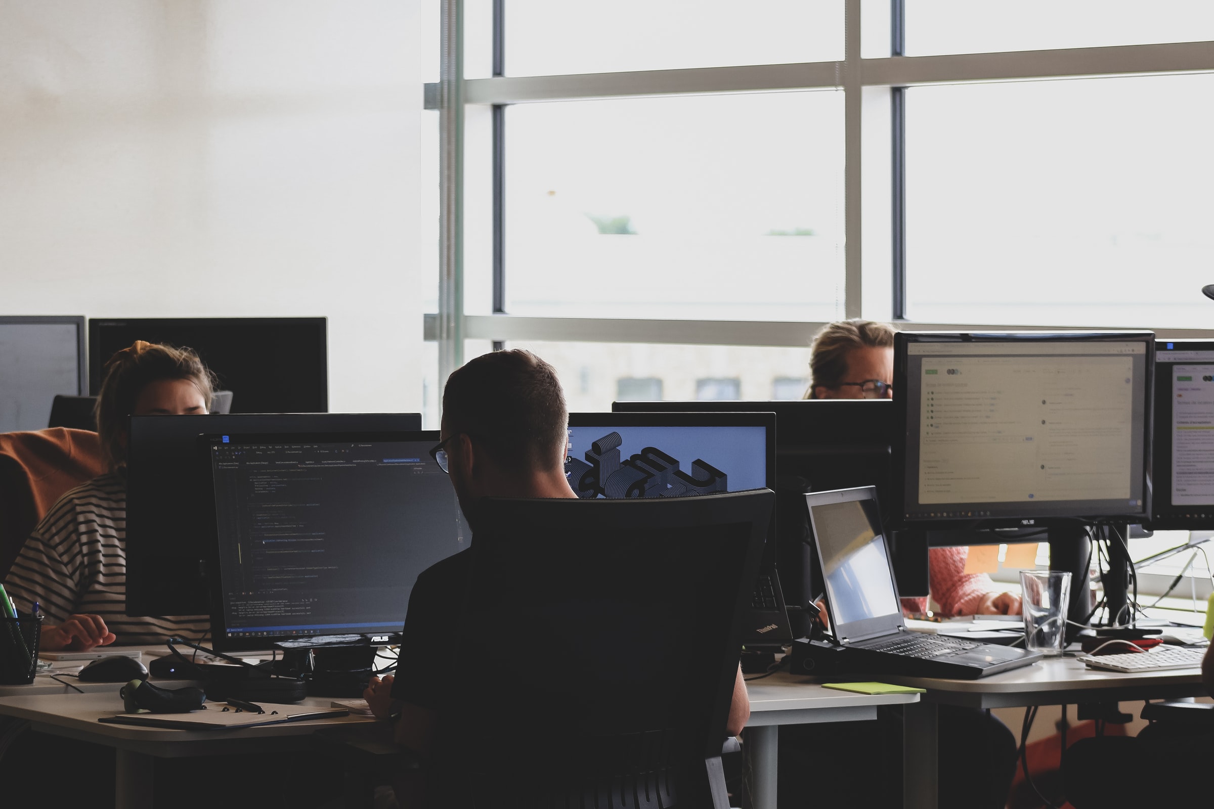 Vemos algumas pessoas em um escritório com vários computadores; todas estão concentradas (imagem ilustrativa).