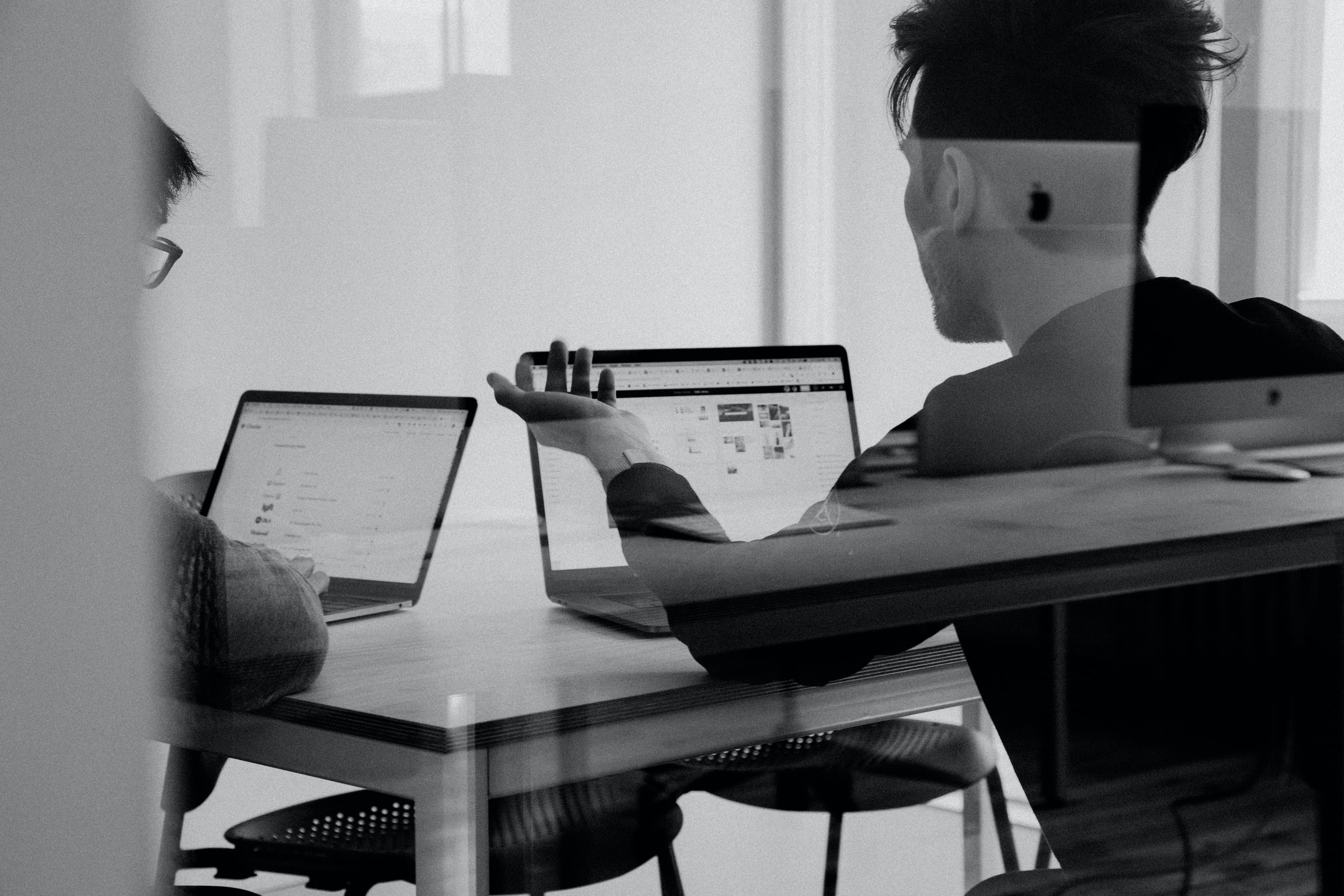 Vemos duas pessoas conversando em um escritório. Sobre a mesa vemos dois computadores (imagem ilustrativa). Texto: startups e corporações.